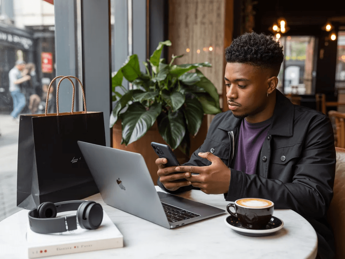 Man using phone in a cafe to compare prices of different products